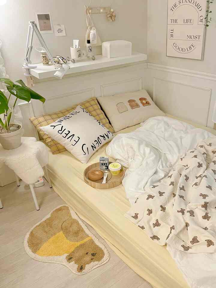 明るいベージュ調の寝室、黄色のマットレスカバーと枕、テディベア柄の掛け布団カバーとかわいいクマ型ラグが配置された雰囲気のある空間