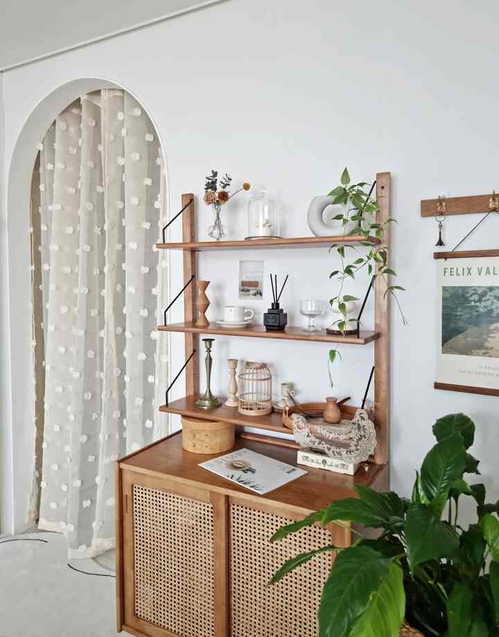 白い壁とアーチ型カーテンがある、飾られた木製の棚と植物が配置された雰囲気のあるナチュラルな空間