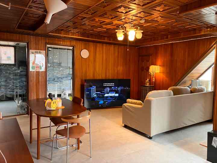 木目調の壁と天井が印象的なリビングとダイニング空間、白いソファとテレビが配置された落ち着いた雰囲気のインテリア