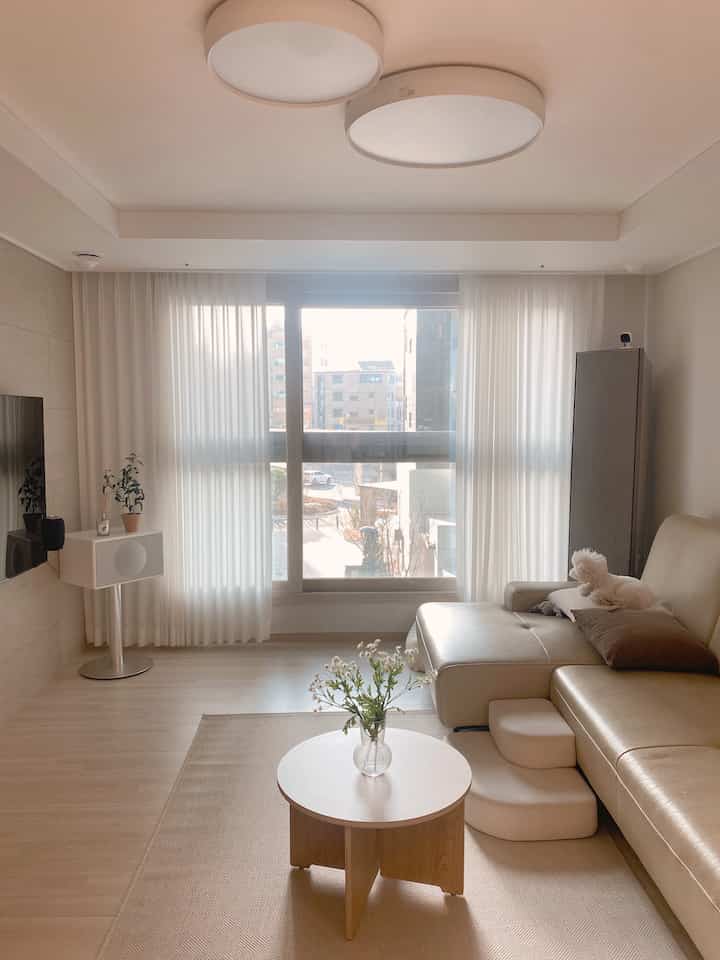 Beige and white toned living room featuring large sofa, round coffee table, and small dog resting on the sofa creating a warm atmosphere