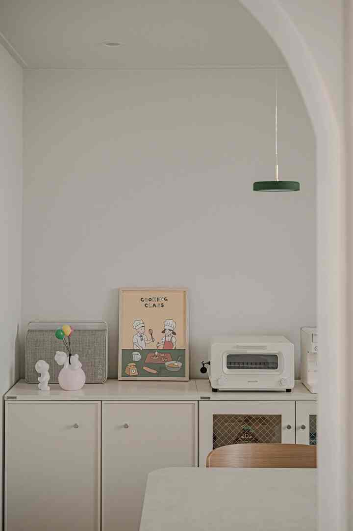 Clean white and wood tone dining room featuring a poster on the wall and kitchen appliances, evoking a natural and calm atmosphere