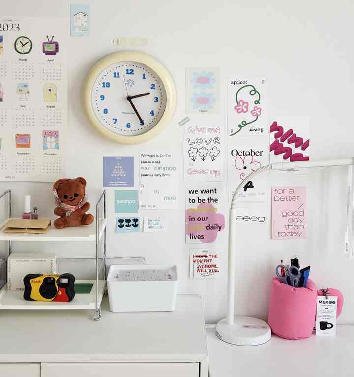 White-toned 6-tatami room featuring a desk, storage shelf, wall clock, and colorful wall prints in a simple home office setup