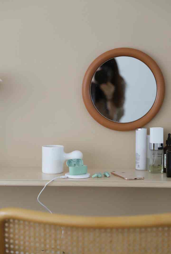 Minimal living space with soft beige wall and round brown frame mirror, small accessories arranged on the vanity table