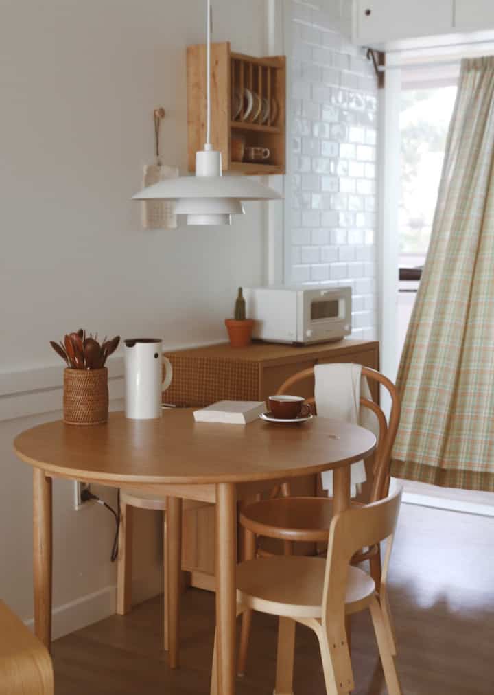 Cozy dining room with warm wood tones and white walls, featuring a round wooden table, chairs, and a yellow check curtain creating a welcoming atmosphere.