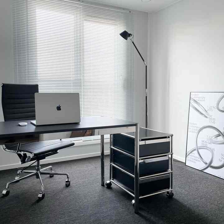 Modern home office space in white and black tones featuring a desk, office chair, and aluminum blinds with a clean atmosphere