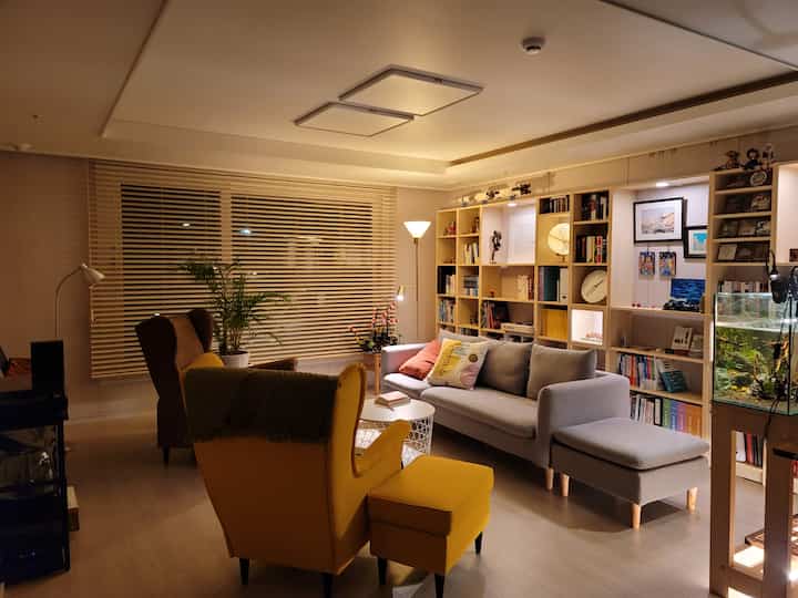 Cozy lit natural modern living room and study space featuring a gray sofa and yellow and brown wing chairs under warm lighting