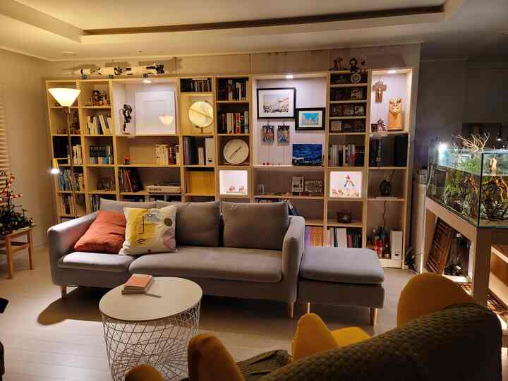 Living room with warm wood tones and natural colors featuring a gray sofa and large bookshelf creating a cozy relaxation space.
