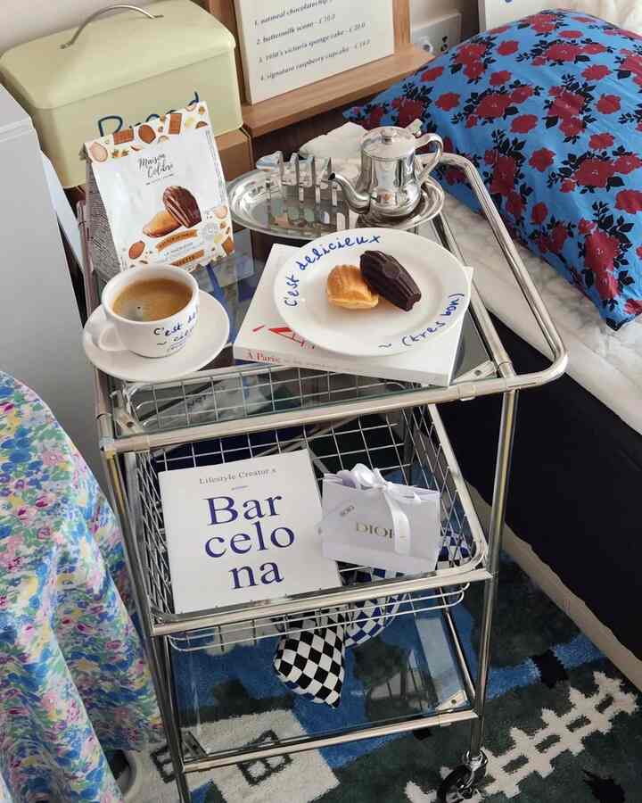 シルバーのステンレス製トレイカートが配置された寝室、ブルーフローラルクッションとコーヒーカップがある雰囲気のあるホームカフェ空間