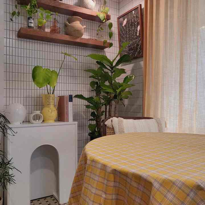 A cozy natural modern dining room with a yellow checkered tablecloth, beige curtains, and green plants blending harmoniously.