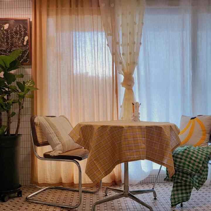 Warm beige and yellow-toned veranda space featuring a round dining table with checkered tablecloth and cushioned chairs, creating a cozy atmosphere