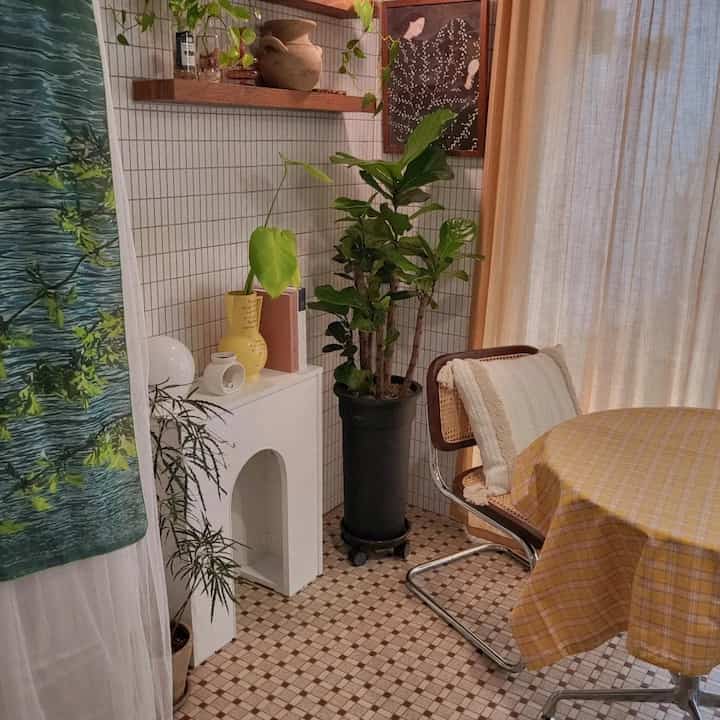 Light beige toned dining room featuring a checkered tablecloth on dining table, chairs, and various plants and objets for a natural cozy atmosphere