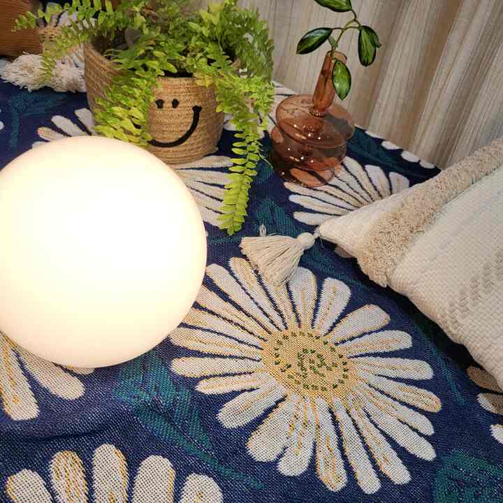ネイビーの背景に白いデイジーパターンが際立つ空間、球状のテーブルランプ、観葉植物、ベージュのクッションとスローが配置された雰囲気のあるインテリア