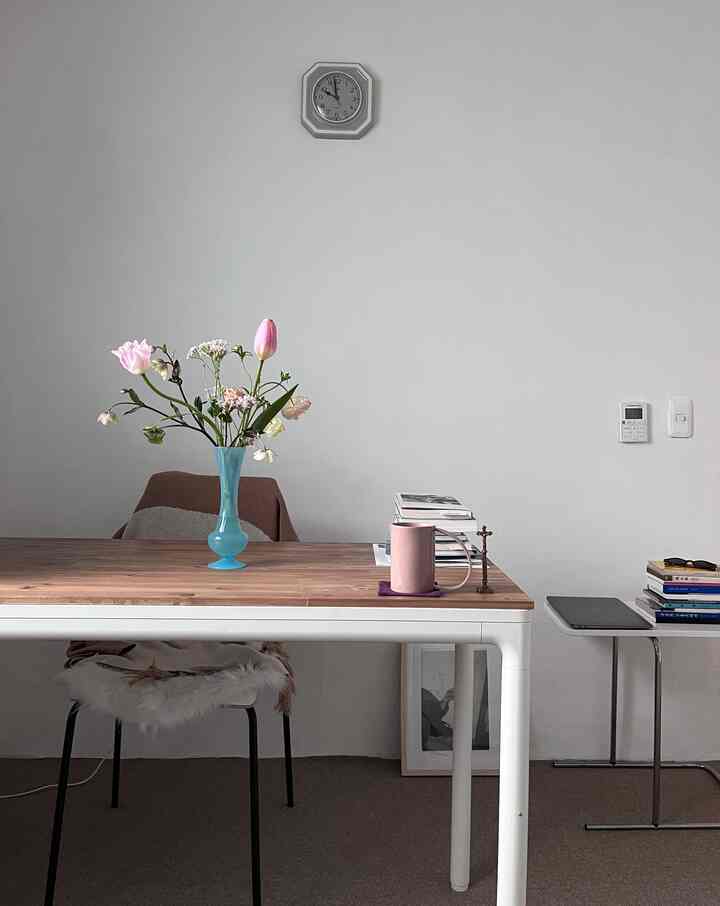 白い壁と茶色の木製テーブルがあるシンプルで落ち着いたダイニング、中央に青い花瓶と花が配置された印象的な空間