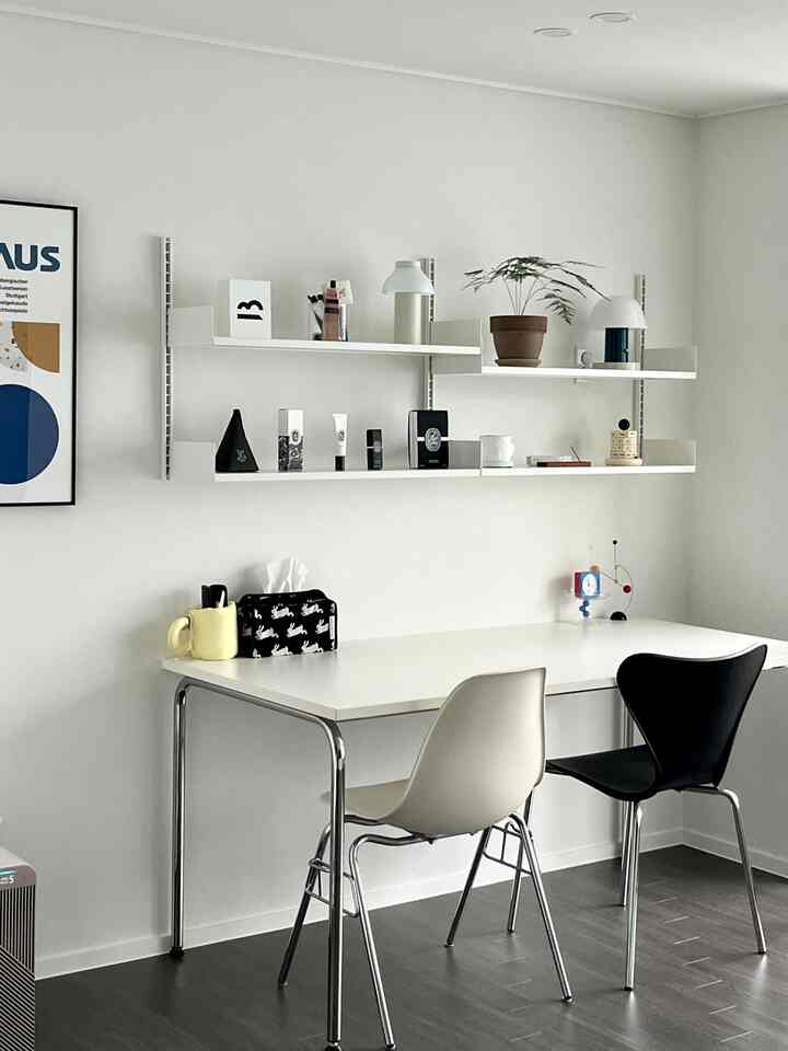 白と黒のトーンが特徴的な二人用のホームオフィス、シンプルな机と椅子、壁に取り付けられた棚に飾られたオブジェが配置された印象的なインテリア