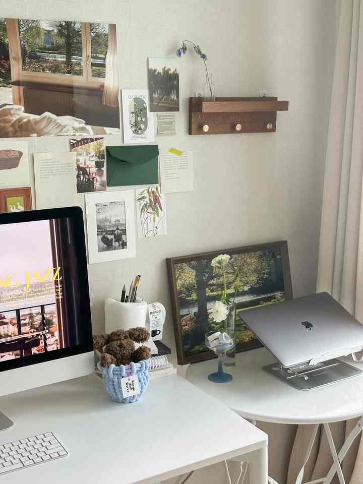 明るい白とブラウンのトーンのホームオフィス、デスクとノートパソコンスタンド、壁に配置された額縁が落ち着いた雰囲気を演出