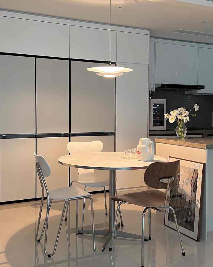 White and light gray toned studio kitchen space featuring a round dining table and assorted dining chairs in a simple modern style