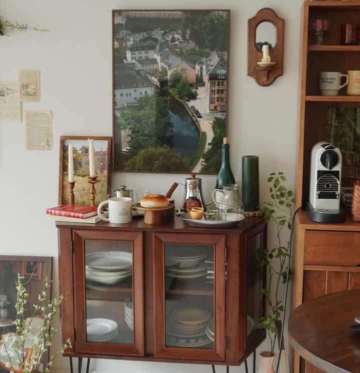 ヴィンテージな木目調のリビングルーム、ガラスキャビネットとコーヒーマシンが配置された居心地の良いおうちカフェ