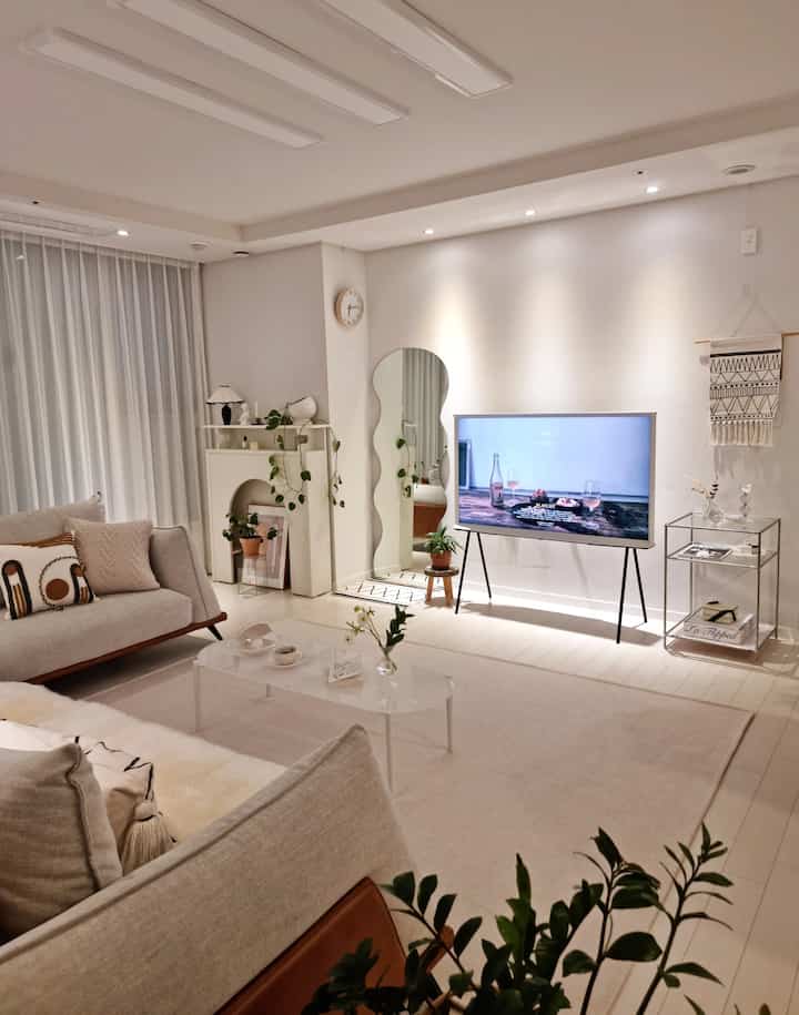 White-toned modern living room featuring mid-century modern sofa, rug, unique wavy mirror, and cozy indirect lighting