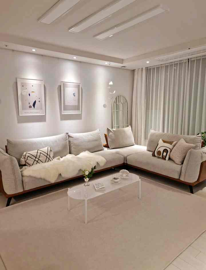 白を基調としたリビング、大型のコーナーソファとラグ、カーテン、額縁が配置されたモダンなインテリア