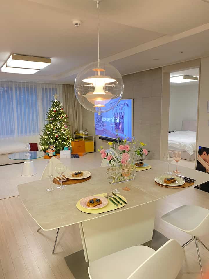 Bright beige and white-toned living room featuring a transparent globe pendant light above a dining table set with vases and plates, creating a clean minimal ambiance