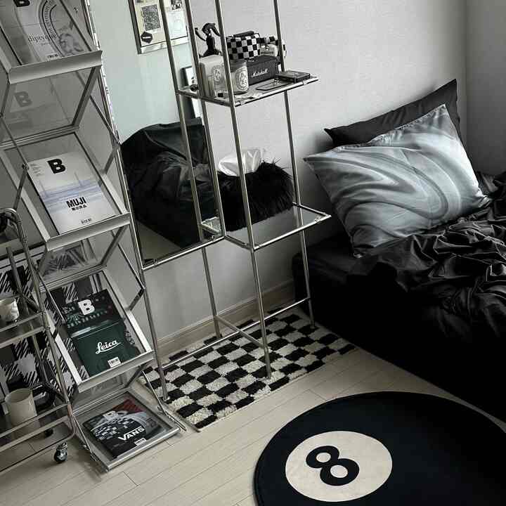 Monotone black and white bedroom featuring checkered and 8-ball rugs, metal shelving, and neatly arranged bedding creating a simple, modern space