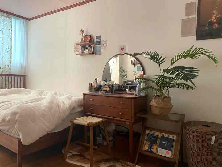 Cozy bedroom with warm brown wood furniture and rattan accents, featuring a vanity, nightstand, and indoor plants