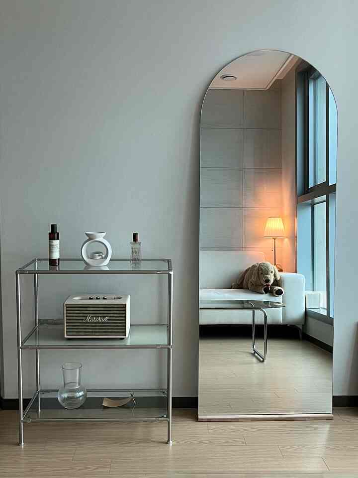 ホワイトとブラウンの色調のリビング、アーチ型の鏡とガラステーブル、ソファが配置されたモダンで洗練されたインテリア