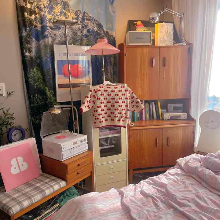A cozy bedroom in pink and white tones featuring wooden cabinets and vintage decor elements