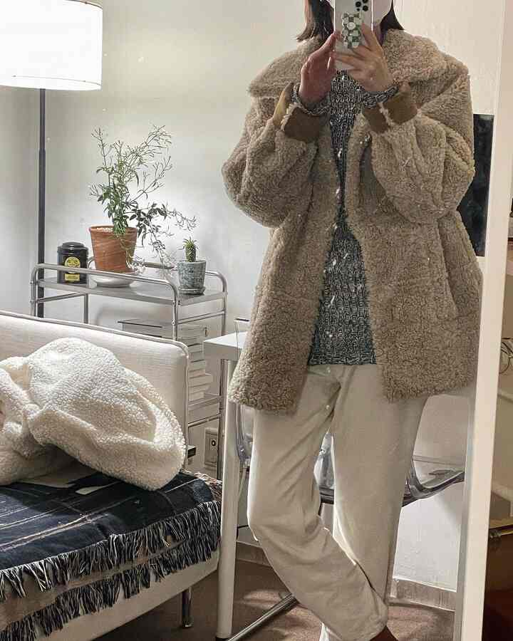 A natural-toned living room in beige and ivory featuring a full-length mirror, sofa, floor lamp, and plants creating a cozy atmosphere