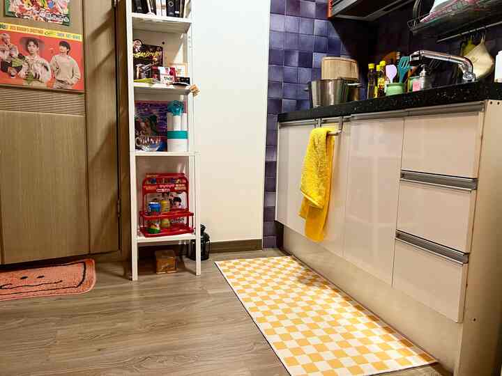 黄色のアクセントがある木目調の床とキッチン家具が配置された狭いキッチンスペース