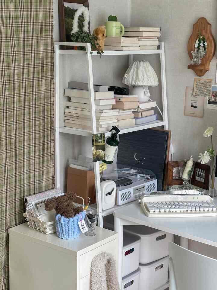 A white and beige toned home office featuring a desk and shelves filled with books and decorative objects, creating a cozy and organized workspace