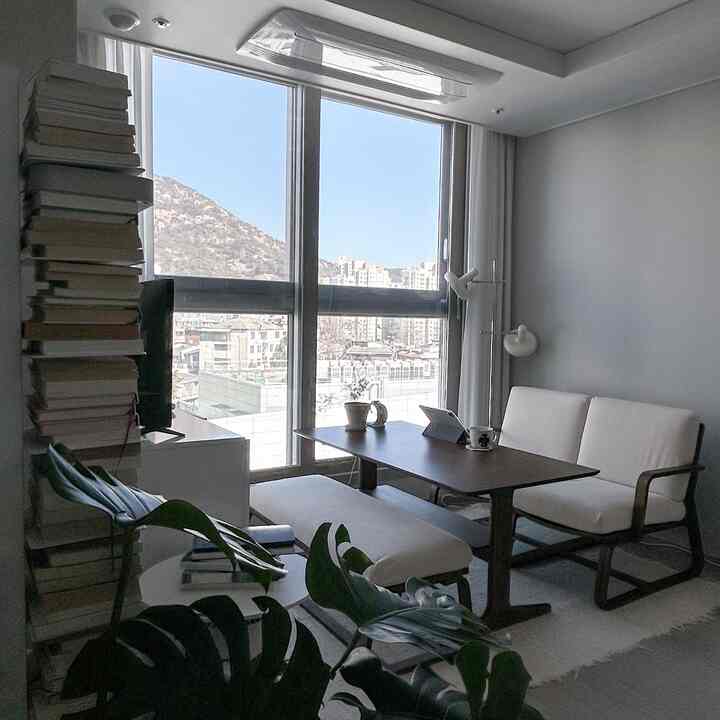 Natural-toned dining room in white and brown, featuring a simple dining table and sofa with large windows and abundant natural light