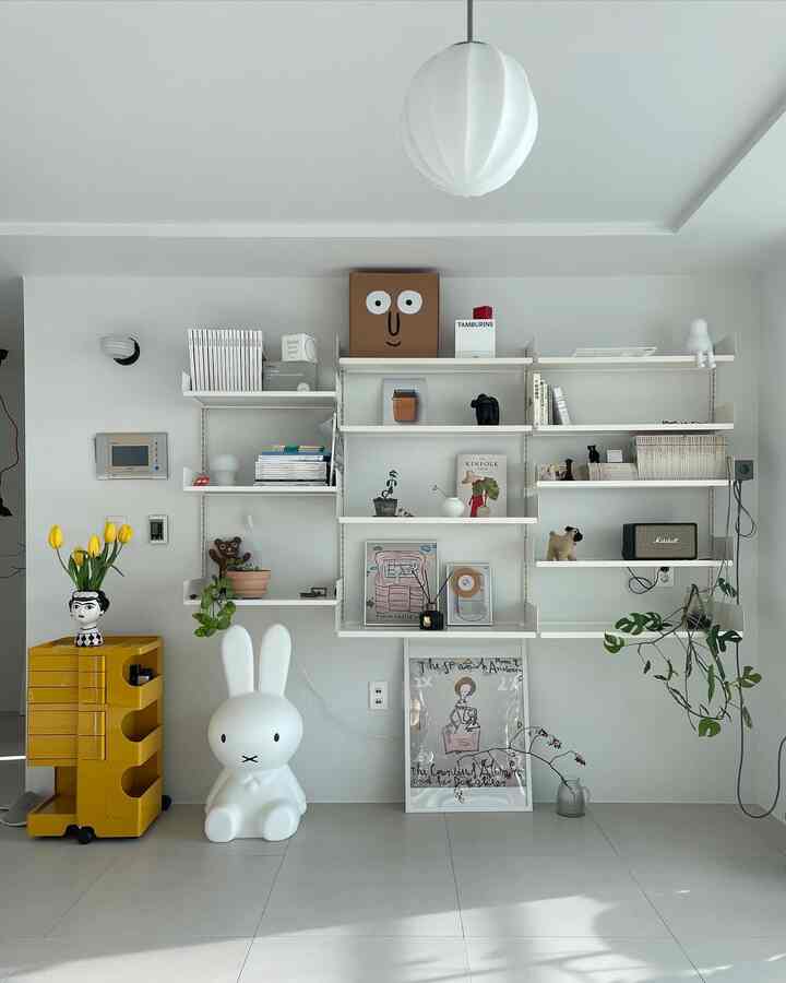 白とナチュラルカラーのリビング、壁掛け棚と多彩な小物が配置された印象的で落ち着いたインテリア