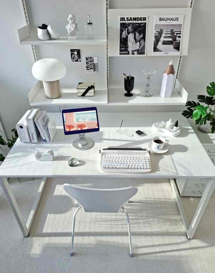 White and gray toned home office featuring a desk with neatly arranged desk supplies and wall shelves in a clean space