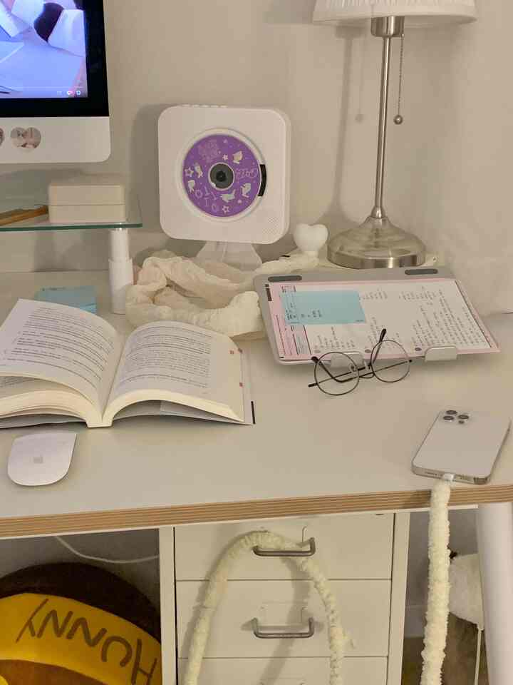 White-toned home office featuring a desk with an open book, CD player, glasses, and desk lamp creating a cozy study area