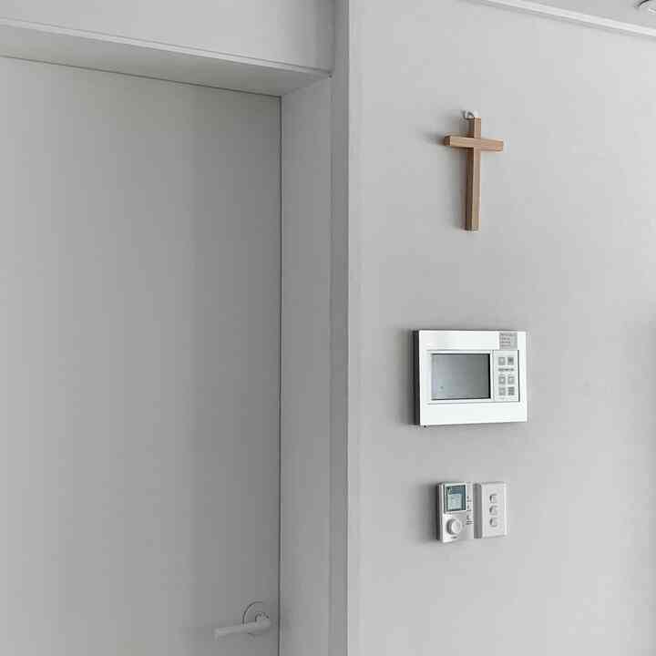 A simple entrance space with bright white walls and door, featuring a wooden cross and intercom with switches centrally mounted on the wall
