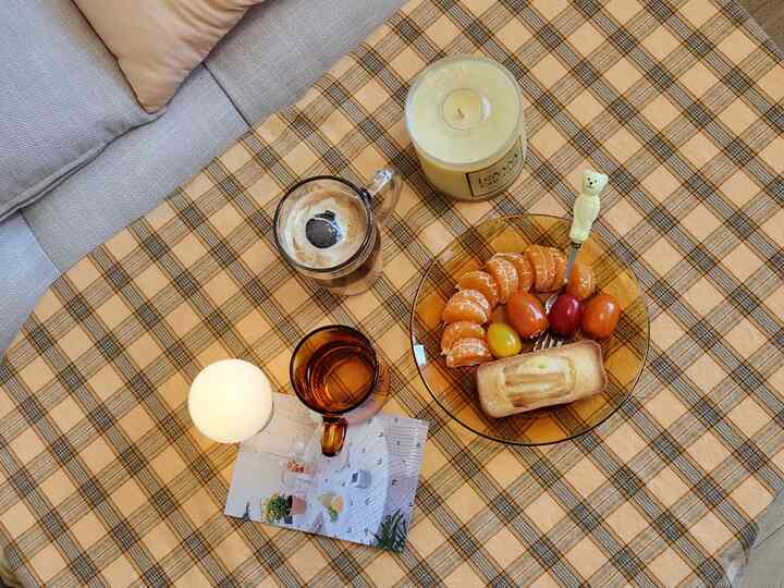 Warm yellow checked tablecloth in living room with sofa, featuring home cafe setup with beverages and snacks in cozy atmosphere