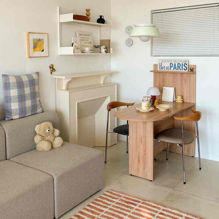 White and beige toned living room featuring beige sofa, wood dining table, pendant light, and blinds creating a cozy space
