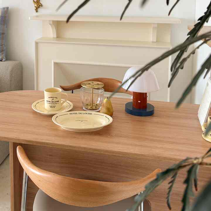 Beige and wood tone dining room featuring a wooden dining table, chairs, table lamp, and tableware in a cozy setting