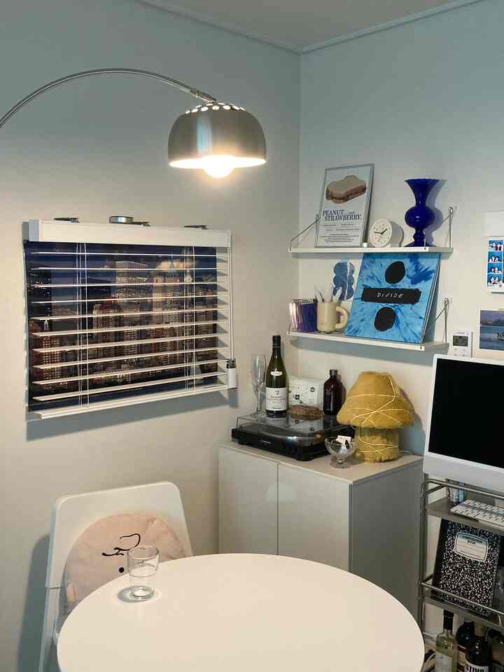 White-toned studio apartment living area featuring a round table, silver floor lamp, and minimal home bar setup