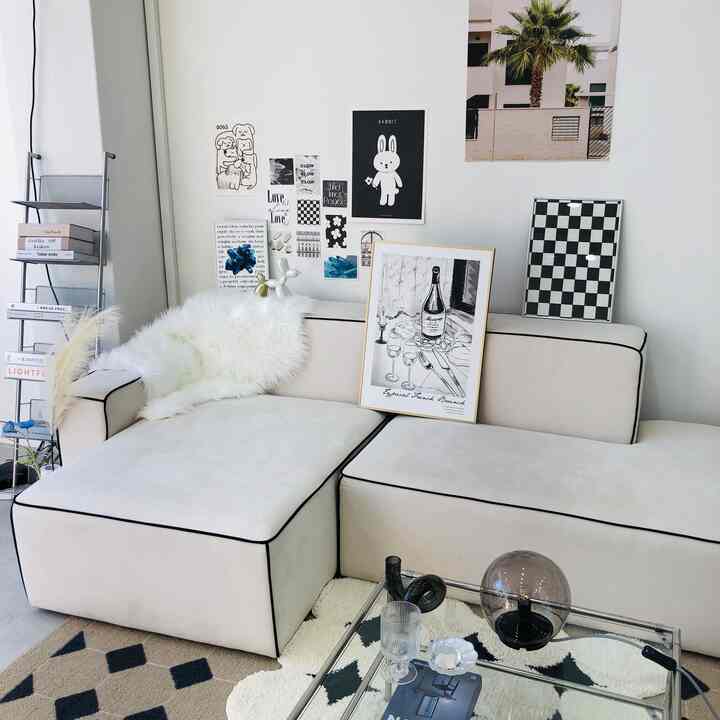 明るいベージュのモノトーンソファと黒縁取り、モノクロのアートポスターが配されたモダンなリビングルーム