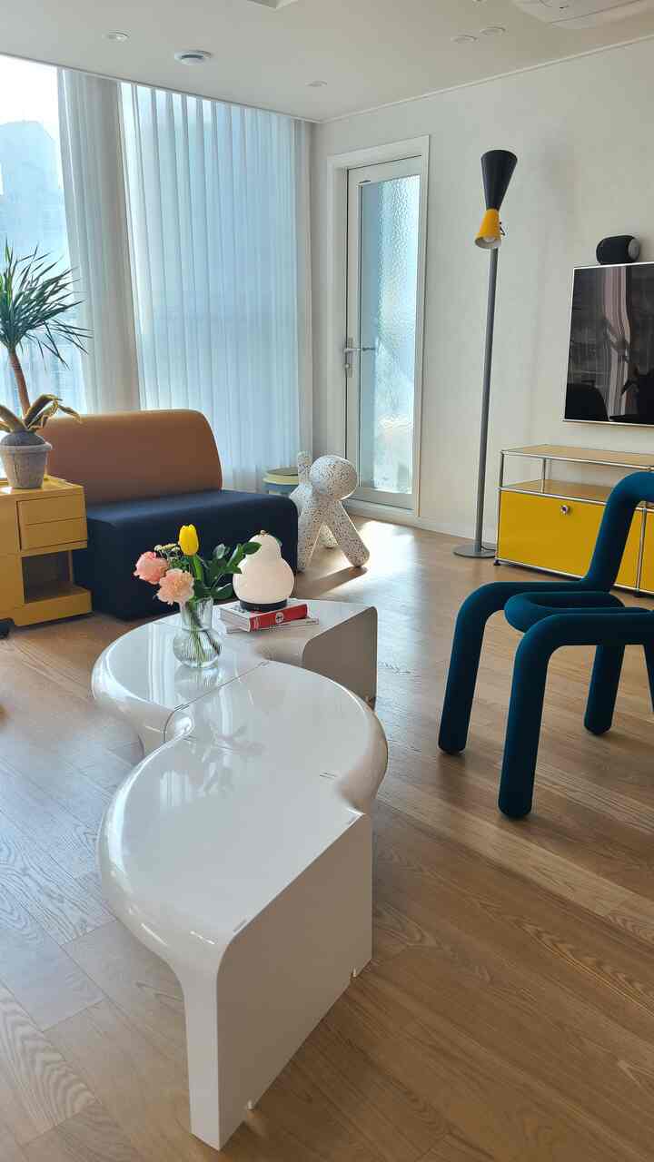 Modern living room with dominant white and wood tones, featuring yellow furniture and blue chairs as visual accents in a bright airy space
