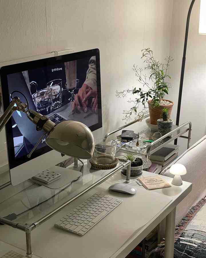 A white and natural tone home office space featuring a desk with computer, floor lamp, and small plants, creating a warm atmosphere