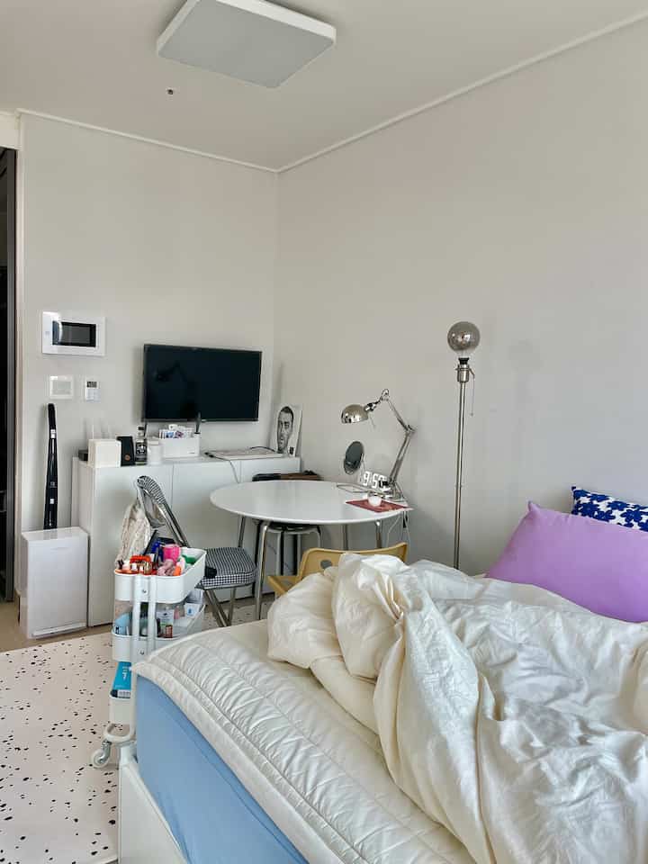 白と青のトーンでまとめられた一人暮らし用のコンパクトな寝室、清潔な寝具と丸テーブルが配置された落ち着いた雰囲気のインテリア