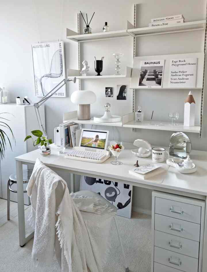 White-toned home office space featuring a desk and shelves with clean, minimal decor