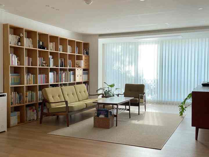 Natural-toned living room featuring large bookshelf, yellow-toned sofa, and sheer curtains with warm cozy atmosphere