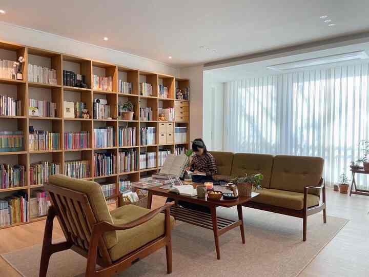 Natural-toned living room with olive green sofa and wooden bookshelf, cozy space with white curtains by the window