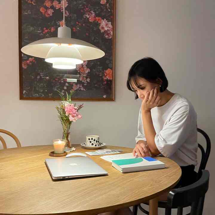 Natural-tone small dining area featuring wooden furniture, pendant light, vase with flowers, and candle creating a cozy atmosphere