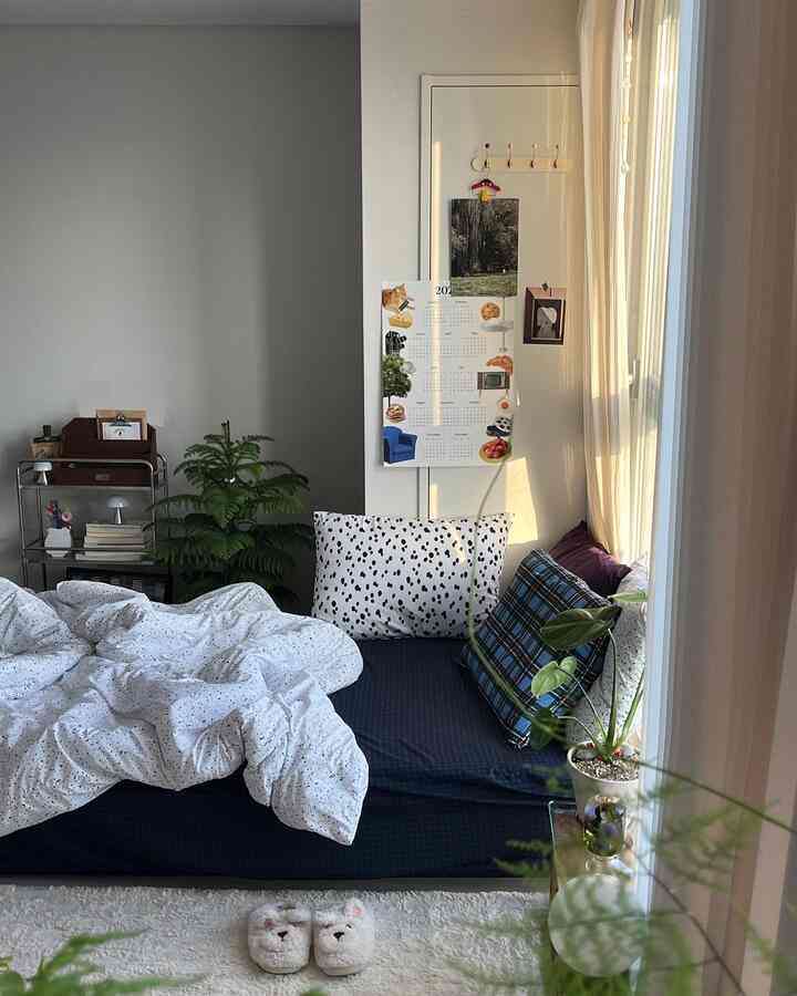 Natural and white toned studio bedroom featuring bedding, curtains, and plants with a cozy atmosphere