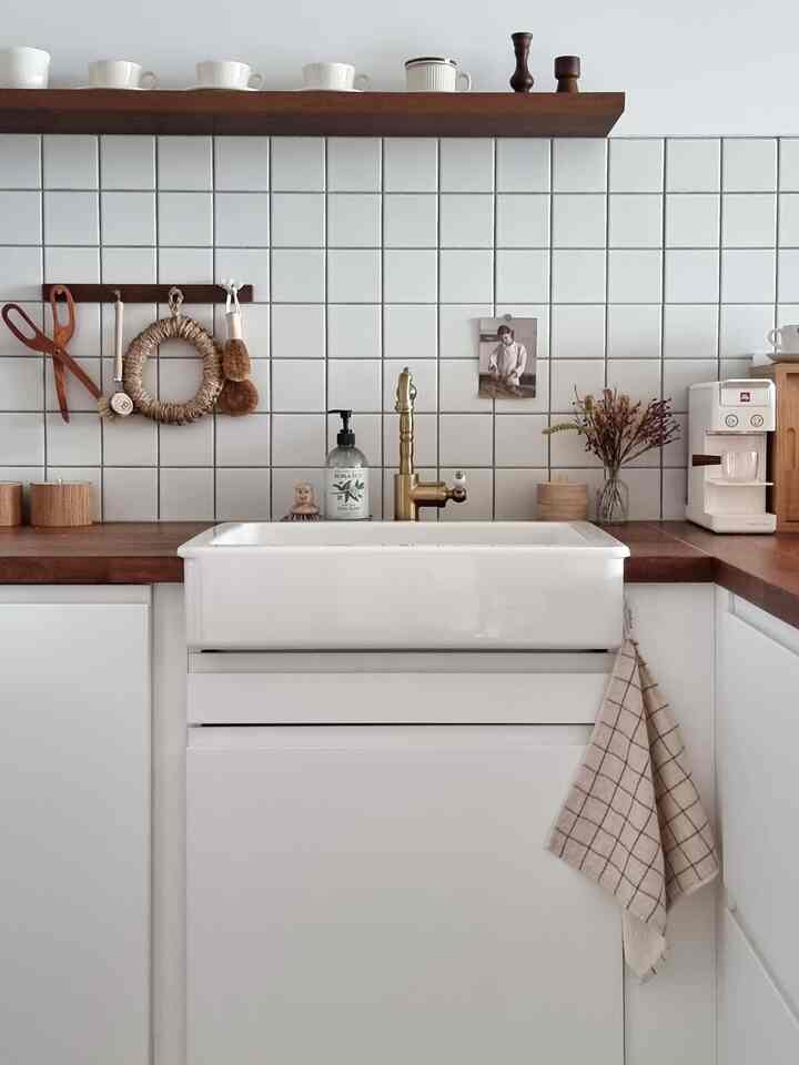 白いタイルの壁と木目調のカウンターに洗練された真鍮の蛇口が調和した清潔感のあるキッチン